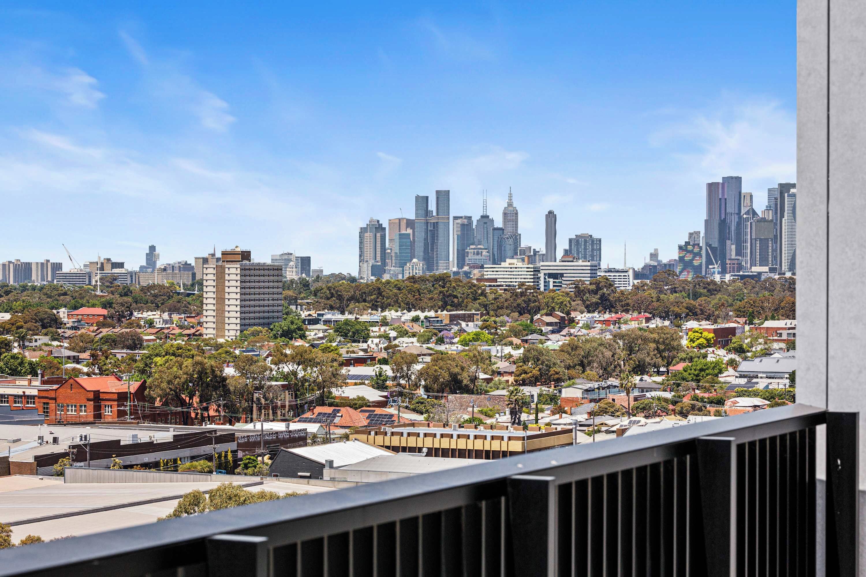 A cityscape with a mix of residential and commercial buildings, a clear sky, and a distant view of a tall skyscraper.
