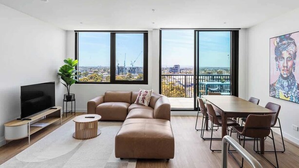 A modern living room with a sectional sofa, a flat-screen TV, a dining table with chairs, and large windows offering a city view. - Family Friendly 3BR Apt with Parking & Workspace (Brunswick)