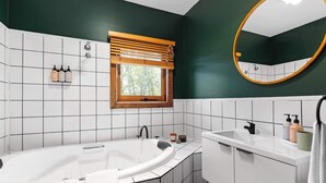 Une salle de bain avec une baignoire sur pieds, une fenêtre avec des stores, un miroir et un lavabo avec des articles de toilette.