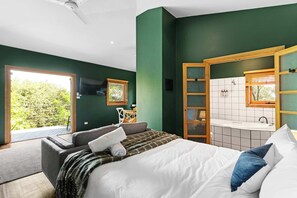 A bedroom with a bed, a sofa, a window, and a bathroom with a sink and mirror. - Daylesford studio with spa bath - walk to town, perfect for couples (Daylesford)
