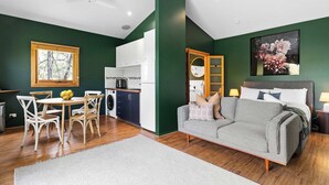 Un salon moderne avec un canapé gris, un coin repas avec des chaises blanches, une cuisine avec des meubles blancs et un mur d’accent vert.