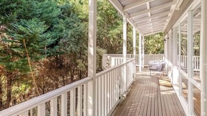 A covered wooden deck with white railings, surrounded by dense green foliage. - Cosy 2 Bedroom Cottage with spabath and fireplace (Kalorama)