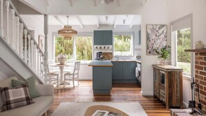 A spacious living area with a staircase, a kitchen with blue cabinets, and a dining area. - Cosy 2 Bedroom Cottage with spabath and fireplace (Kalorama)