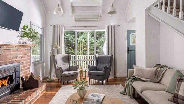 A living room with a fireplace, two armchairs, a sofa, a coffee table, and a large window with curtains. - Cosy 2 Bedroom Cottage with spabath and fireplace (Kalorama)