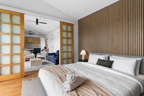 Ein modernes Hotelzimmer mit einem großen Bett, Holzboden, einer Schiebetür aus Glas zum Essbereich und einem Deckenventilator.