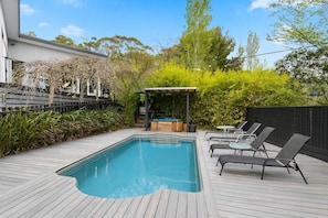 Ein rechteckiger Pool mit Holzterrasse, Whirlpool und Liegestühlen.