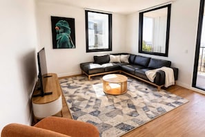 Ein modernes Wohnzimmer mit einem Ecksofa, einem Couchtisch, einem Fernseher und einem großen Fenster.