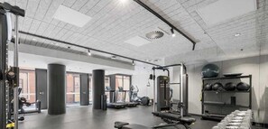 Une salle de sport équipée de tapis de course, d’appareils de musculation et d’un mur rempli de ballons médicinaux.