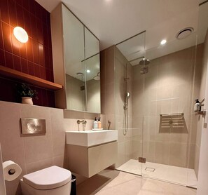 A modern bathroom with a toilet, sink, mirror, shower, and a towel rack. - Brunswick 2BR 2Bath w Free Parking + Park Views (Brunswick)