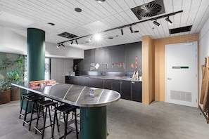 Un área de cocina moderna con una isla de acero inoxidable, taburetes de bar y un panel perforado con herramientas.