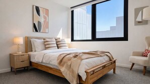 A bedroom with a bed, bedside tables, a chair, a window, and a wall art piece. - Brunswick 2BR 2Bath w Free Parking + Park Views (Brunswick)