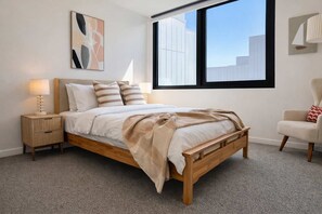 A bedroom with a bed, bedside tables, a chair, a window, and a wall art piece. - Brunswick 2BR 2Bath w Free Parking + Park Views (Brunswick)
