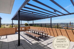 A covered outdoor seating area with tables and benches, a grill, and a brick wall. - Brunswick 2BR 2Bath w Free Parking + Park Views (Brunswick)