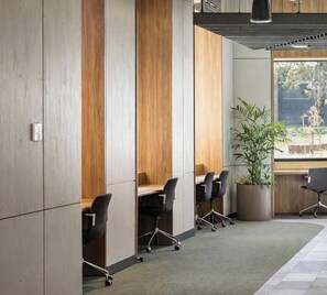 Een moderne kantoorruimte met houten lambrisering, een groot raam met uitzicht op groen en een verlaagd plafond met een lange lichtbalk.