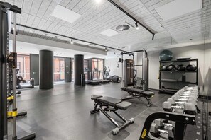 Ein Fitnessstudio mit Trainingsgeräten, Laufbändern und einer Wand mit Kurzhanteln.