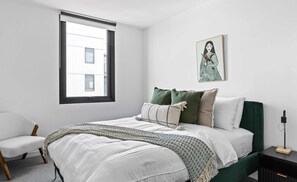 A bedroom with a bed, a chair, a window, a painting, and a nightstand. - City View 3BR | Free Parking | Family Friendly (Brunswick)