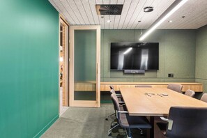 A conference room with a large flat-screen TV mounted on the wall, a long wooden table with chairs, and a sliding door leading to another room. - Cityscape 901 | Top-Floor City View, Brunswick 3BR (Brunswick)