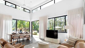 Amplia sala de estar con una mesa de comedor, asientos cómodos, un televisor de pantalla plana y ventanas grandes que ofrecen vistas a zonas verdes.