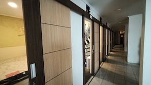 A hallway with a wooden floor, a tiled wall, and a door with a decorative pattern. - Stadio Hostel (Kota Yogyakarta)