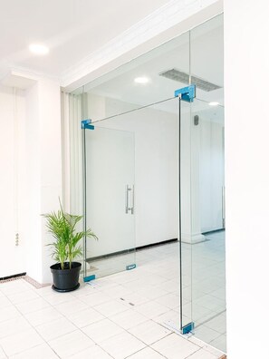 A modern interior with a glass partition, a potted plant, and a tiled floor. - Stadio Hostel (Yogyakarta)