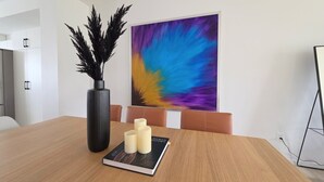 Een vergaderruimte met een houten tafel, een zwarte vaas met decoratieve takken, een boek getiteld 'HUMAN VISION' en een kleurrijk abstract schilderij aan de muur.