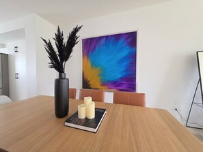 Ein Konferenzraum mit einem Holztisch, einer schwarzen Vase mit dekorativen Zweigen, einem Buch mit dem Titel 'HUMAN VISION' und einem farbenfrohen, abstrakten Gemälde an der Wand.