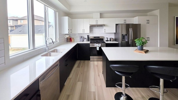 Een moderne keuken met witte kasten, roestvrijstalen apparatuur en een groot kookeiland met barstoelen.