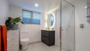 Ein modernes Badezimmer mit Toilette, Waschbecken mit Spiegel, Dusche und einer Pflanze.