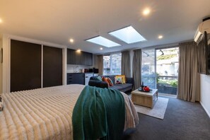 A bedroom with a large bed, a sofa, a small table, and a balcony with a view. - Bright Modern Guesthouse - Free Parking, Near CBD (Christchurch)