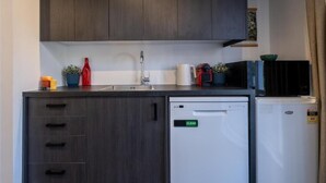 Eine kleine Küche mit dunklen Schränken, einem Geschirrspüler, einem Kühlschrank und einer Spüle.