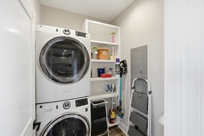 A laundry room with stacked washers and dryers, a shelf with various items, and a door to another room. - New St George Island Retreat  Pool Pet Friendly (Saint George Island)
