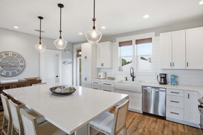A modern kitchen with white cabinetry, a central island with seating, pendant lighting, and a large wall clock.