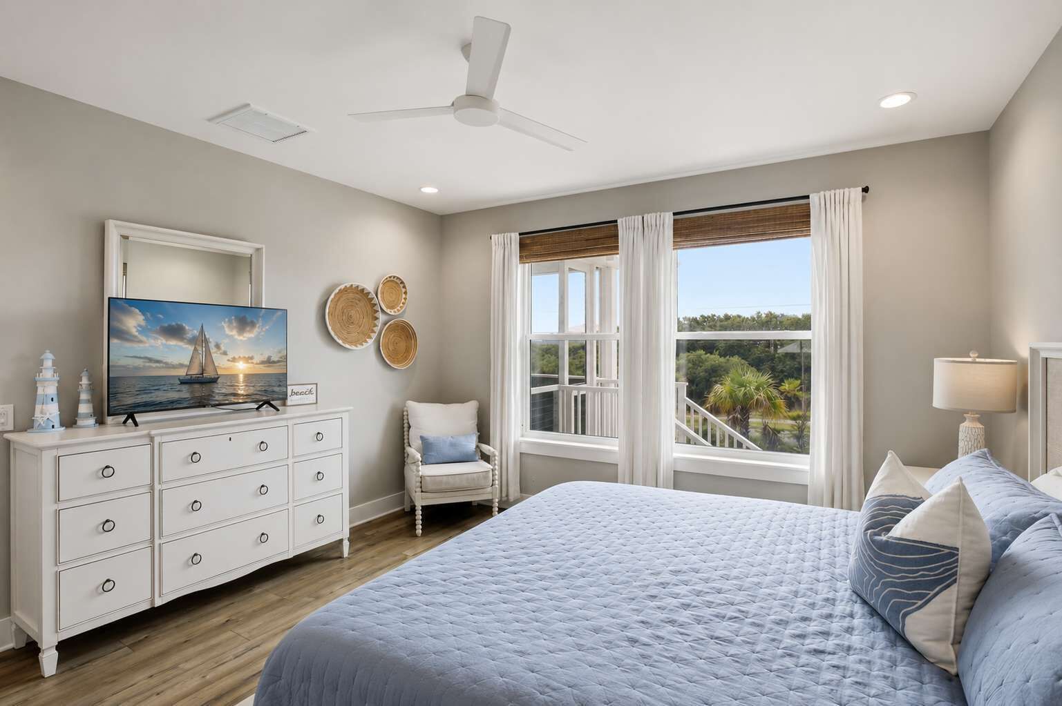 A bedroom with a bed, a dresser, a chair, a television, and a view of the outdoors.