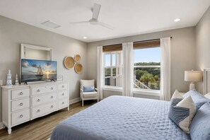 A bedroom with a bed, a dresser, a chair, a television, and a view of the outdoors.