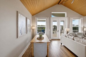 A spacious living area with a high ceiling, a dining table with chairs, a sofa, and large windows offering views of the outdoors. - New St George Island Retreat  Pool Pet Friendly (Saint George Island)