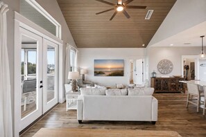 A spacious living room with a large white sofa, a ceiling fan, and a painting of a sunset.