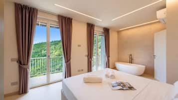 Ein modernes Hotelzimmer mit einem großen Bett, einer Badewanne und einem Balkon mit Vorhängen.