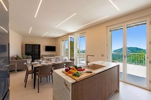 A modern kitchen with a central island, dining area, and a balcony with a view.