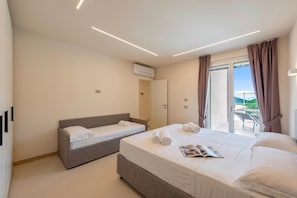Ein Hotelzimmer mit Bett, Schlafsofa, Balkon mit Tisch und Stühlen sowie Klimaanlage.