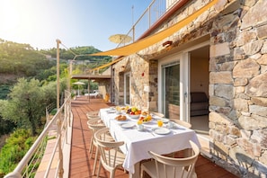 A terrace with a table set for breakfast, stone walls, and a view of the surrounding landscape.