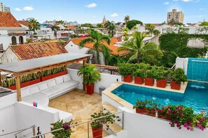 A rooftop terrace with a pool, white outdoor furniture, potted plants, and a view of the cityscape. - Casa Milagros | Oasis en la Ciudad Amurallada (Cartagena)