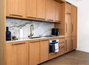 A kitchen with wooden cabinets, a marble countertop, a sink, a coffee maker, and an oven. - The Gallery | Lux Studio in Wynwood (Miami)