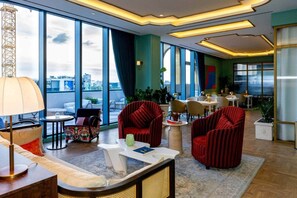 A modern hotel lobby with a large window, red upholstered chairs, a round table, and a bar area. - The Gallery | Lux Studio in Wynwood (Miami)