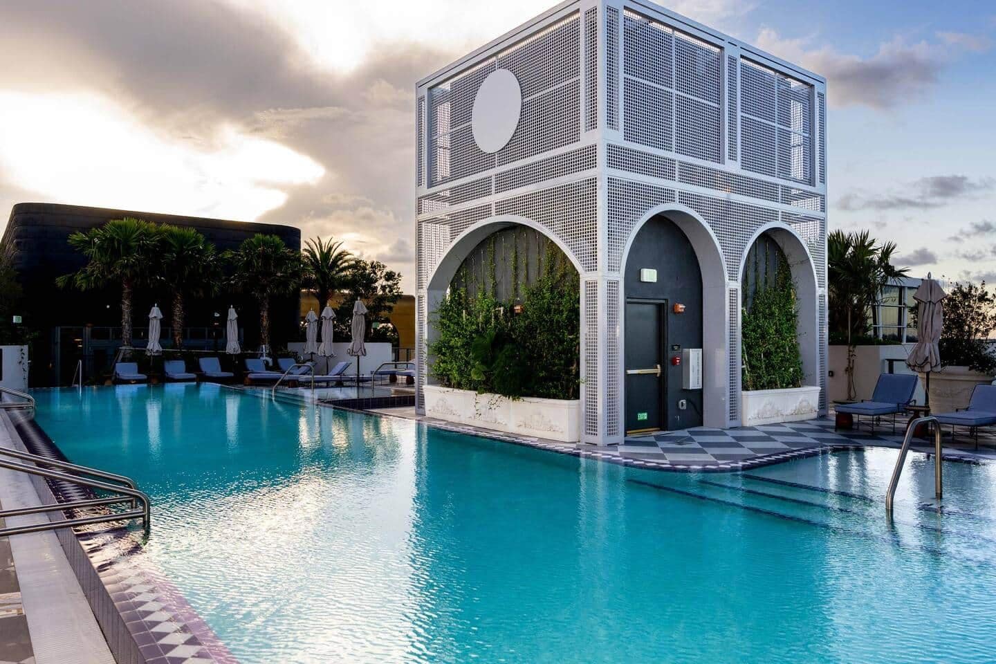 A swimming pool with lounge chairs and a modern building with arched windows.