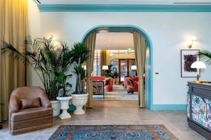 A spacious lobby with a brown leather armchair, potted plants, a colorful rug, and a view into a dining area with red furniture. - The Gallery | Lux Studio in Wynwood (Miami)