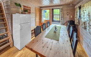 A wooden cabin interior with a dining table, chairs, a refrigerator, a ladder, and a window with a view of greenery. - Stunning home in Tjørhom with sauna (Tjørhom)