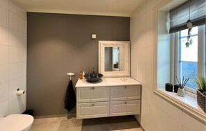 Un bagno con un mobile lavabo bianco, uno specchio grande, una finestra con persiane e un water.