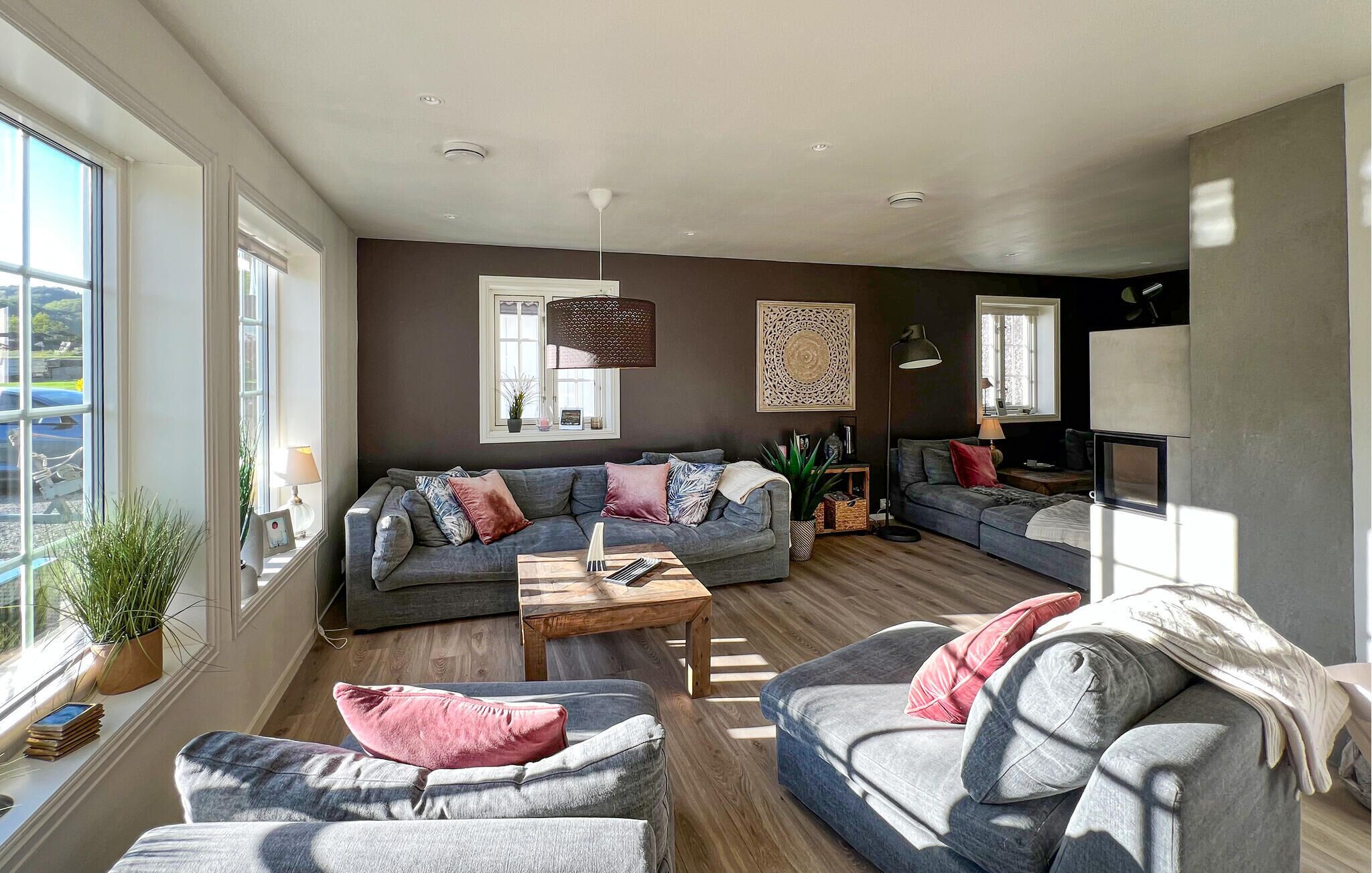 A modern living room with a grey sofa, a wooden coffee table, and a large window providing natural light.