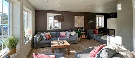 A modern living room with a grey sofa, a wooden coffee table, and a large window providing natural light.