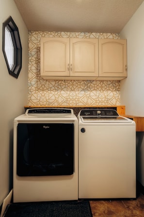 Une cuisine compacte équipée d’un lave-linge et d’un sèche-linge, de meubles en bois et d’un crédence décorée.
